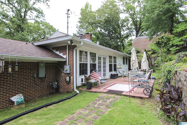 back of house with roof with shingles, brick siding, a yard, a patio, and a chimney