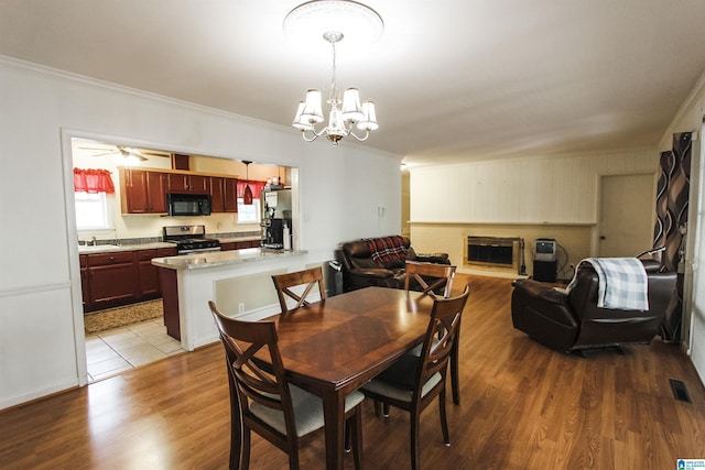 dining space with ornamental molding, visible vents, ceiling fan with notable chandelier, a brick fireplace, and wood finished floors