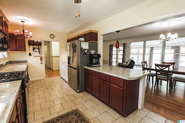 kitchen featuring a peninsula, light tile patterned floors, stainless steel appliances, and a notable chandelier