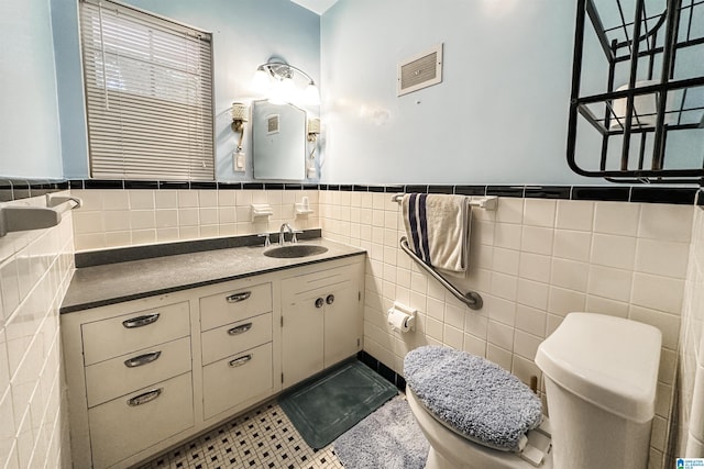 bathroom featuring tile walls, toilet, wainscoting, visible vents, and vanity
