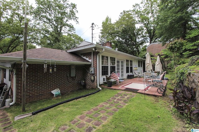 back of house featuring french doors, a chimney, a lawn, a deck, and brick siding