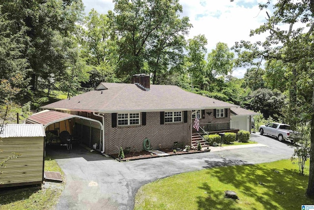 view of front of house with a chimney, driveway, brick siding, a front yard, and roof with shingles