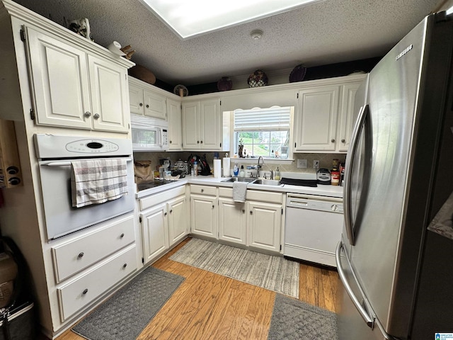 kitchen featuring a sink, white appliances, a textured ceiling, light wood-style flooring, and white cabinets