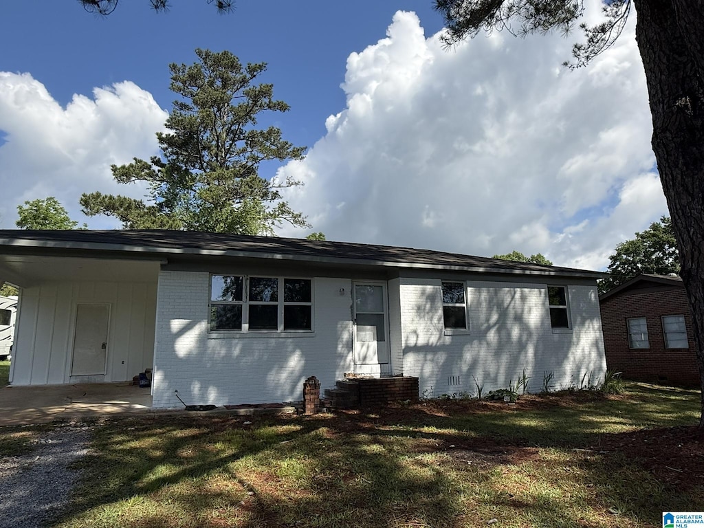 single story home with entry steps, an attached carport, brick siding, and a front lawn