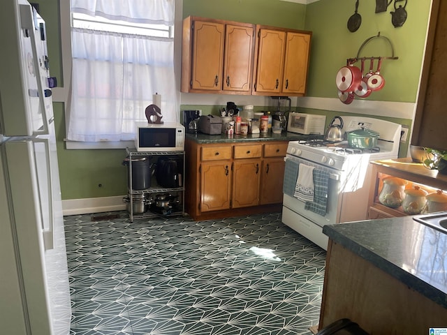 2121 47th Pl, Birmingham, AL 35208 - kitchen featuring dark countertops, baseboards, brown cabinets, and white appliances