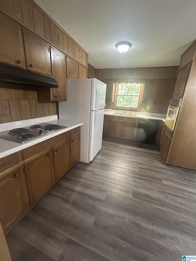 kitchen featuring under cabinet range hood, a textured ceiling, white appliances, and a sink