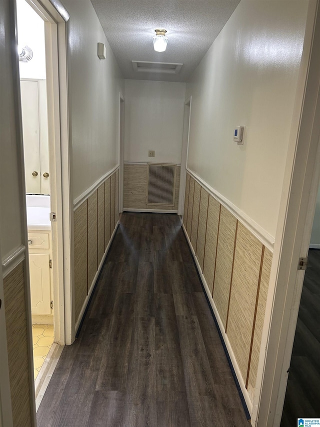 hall with a textured ceiling, visible vents, wood walls, wainscoting, and dark wood-style floors