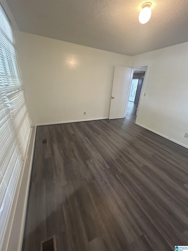 unfurnished room featuring baseboards, visible vents, a textured ceiling, and dark wood-type flooring