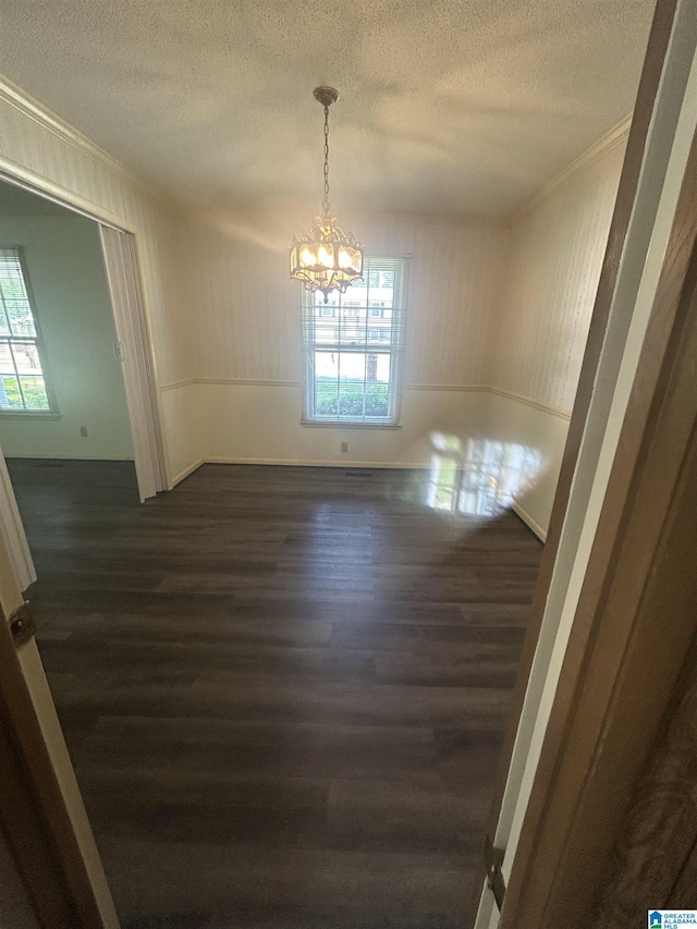 unfurnished dining area with a textured ceiling, dark wood-type flooring, and ornamental molding