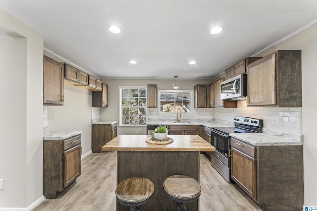kitchen with light wood finished floors, a sink, a kitchen island, backsplash, and appliances with stainless steel finishes