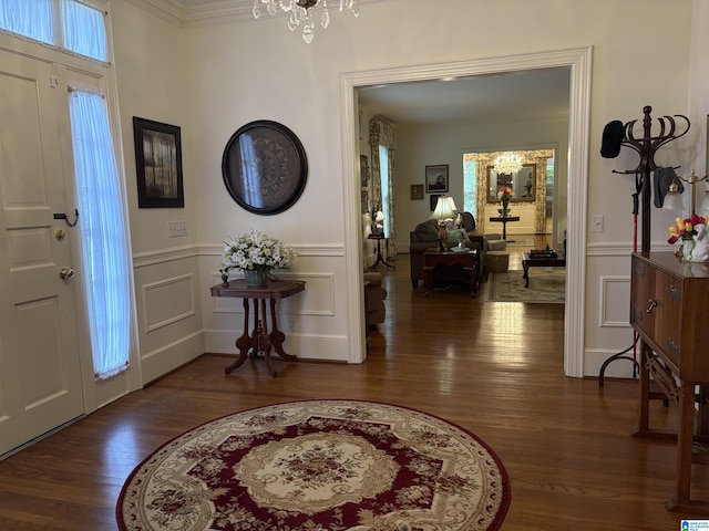 entryway with ornamental molding, a chandelier, a decorative wall, and wood finished floors