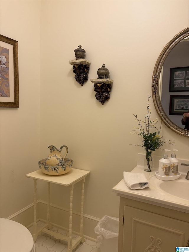 half bathroom featuring tile patterned floors, toilet, baseboards, and vanity