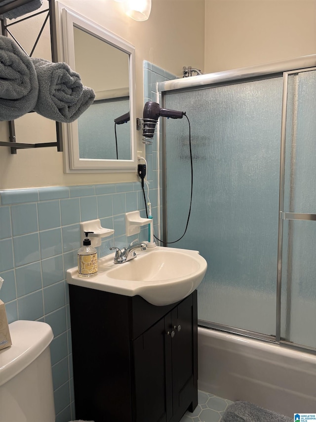 bathroom featuring toilet, tile walls, wainscoting, bath / shower combo with glass door, and vanity
