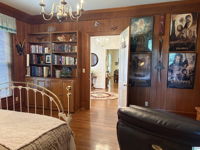 bedroom featuring a chandelier, ornamental molding, wooden walls, and wood finished floors