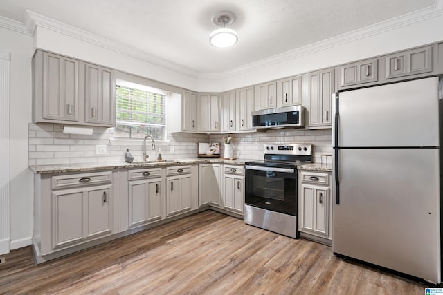 816 8th Cir N, Pell City, AL 35125 - kitchen featuring appliances with stainless steel finishes, a sink, ornamental molding, light wood-type flooring, and light stone countertops
