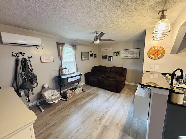 living room featuring a textured ceiling, light wood finished floors, a wall mounted AC, a ceiling fan, and baseboards