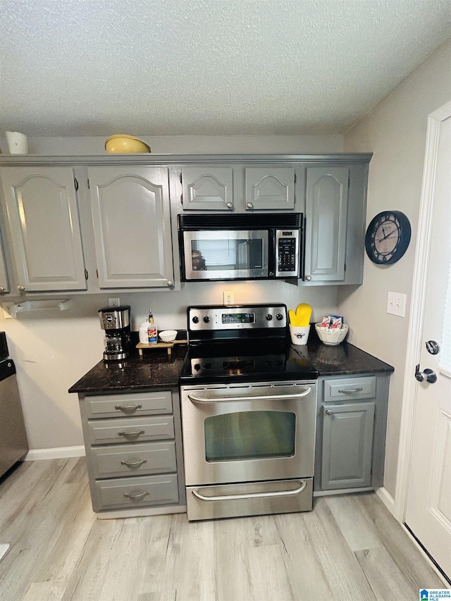 kitchen with a textured ceiling, light wood-style floors, stainless steel appliances, and gray cabinets