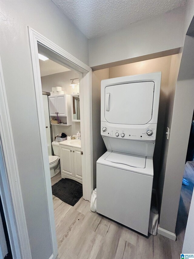 laundry area with a sink, laundry area, stacked washing maching and dryer, a textured ceiling, and light wood-type flooring