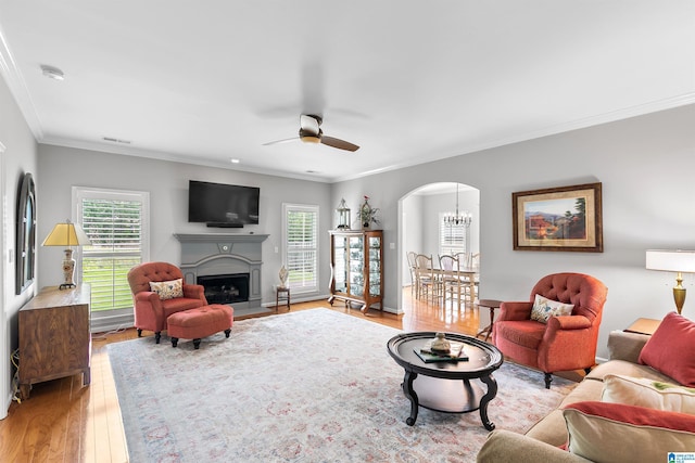 living area with arched walkways, plenty of natural light, ceiling fan, light wood finished floors, and crown molding
