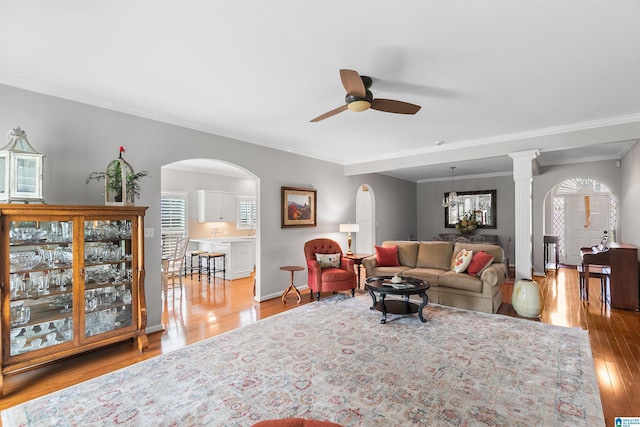 living room featuring a ceiling fan, wood finished floors, crown molding, arched walkways, and baseboards