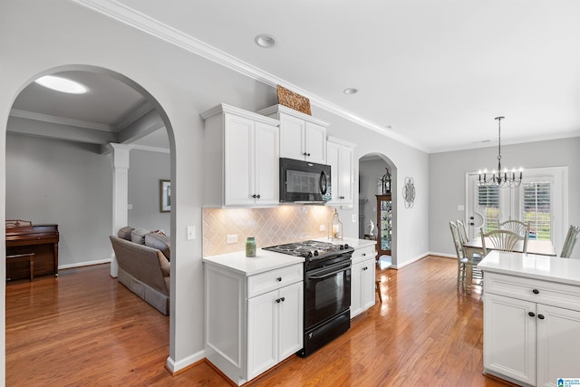 kitchen featuring black appliances, arched walkways, light countertops, light wood finished floors, and backsplash