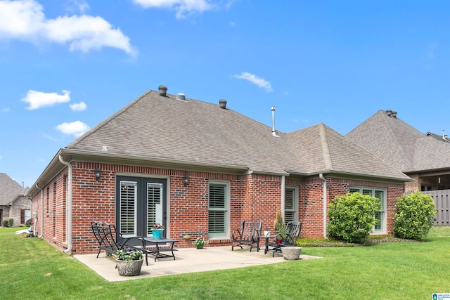 rear view of property with brick siding, roof with shingles, a lawn, and a patio area