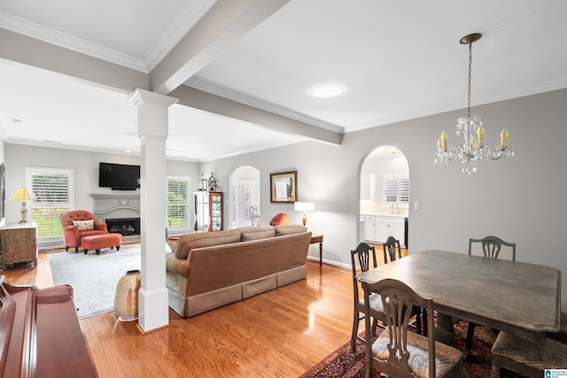 living room with a fireplace, light wood finished floors, crown molding, arched walkways, and baseboards