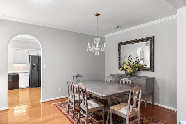 dining area featuring ornamental molding, a chandelier, light wood-style flooring, baseboards, and arched walkways
