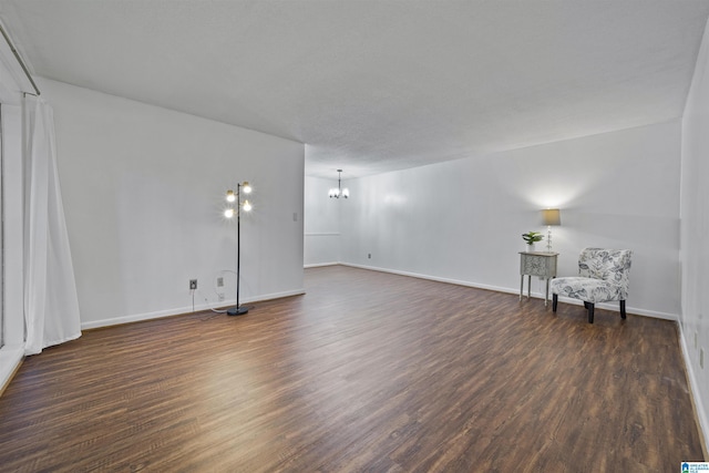 unfurnished room with dark wood-type flooring, a chandelier, and baseboards