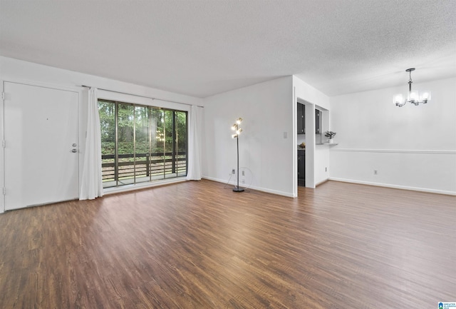 unfurnished living room with wood finished floors, a chandelier, a textured ceiling, and baseboards