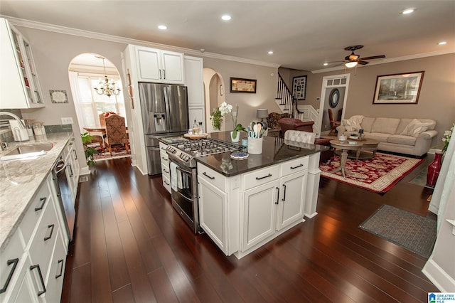kitchen with a sink, ceiling fan with notable chandelier, dark stone countertops, arched walkways, and appliances with stainless steel finishes