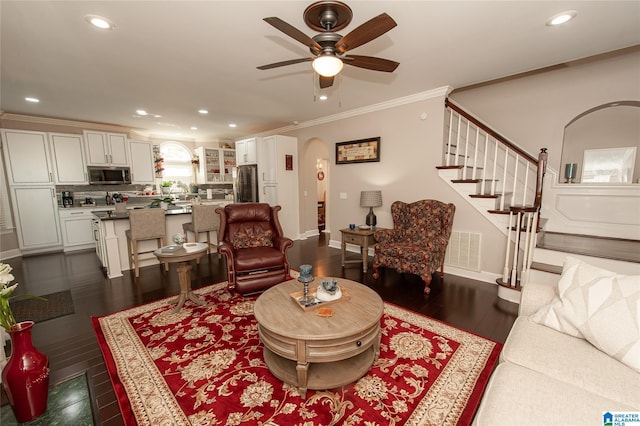 living room with visible vents, dark wood-style flooring, crown molding, arched walkways, and a ceiling fan