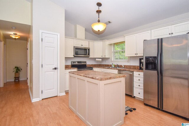 kitchen with stainless steel appliances, light wood-style flooring, white cabinets, decorative light fixtures, and vaulted ceiling
