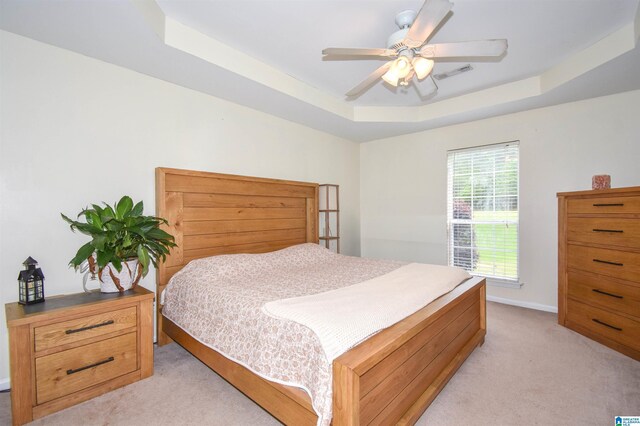 bedroom with a tray ceiling, light carpet, baseboards, and ceiling fan