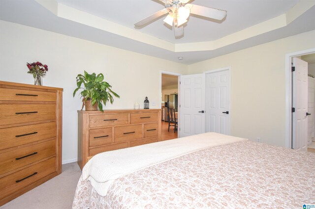 bedroom with a tray ceiling, stainless steel fridge, light colored carpet, and a ceiling fan