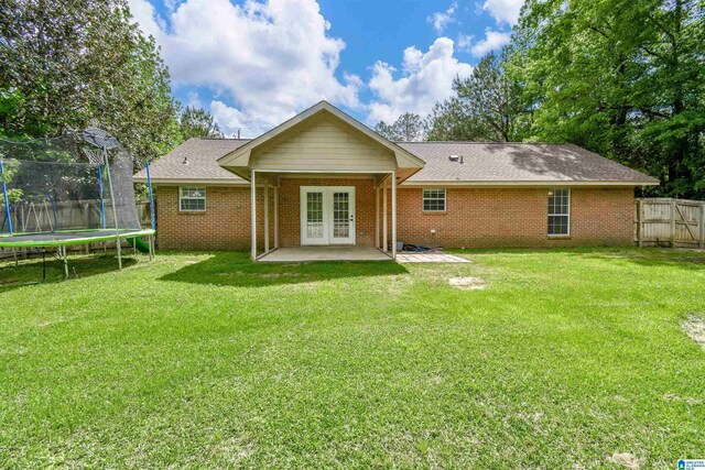 rear view of property featuring french doors, a trampoline, a patio area, brick siding, and a shingled roof