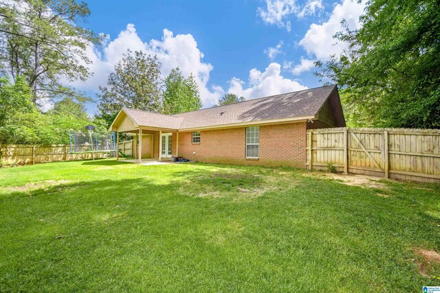 rear view of property featuring a trampoline, brick siding, french doors, a patio, and roof with shingles