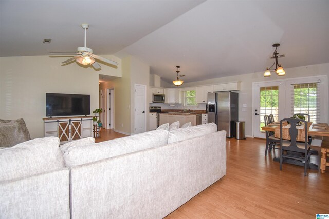 living area with lofted ceiling, a ceiling fan, light wood-style floors, and baseboards
