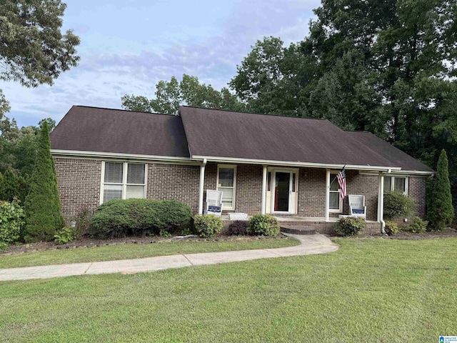 single story home featuring a porch, a shingled roof, brick siding, and a front lawn