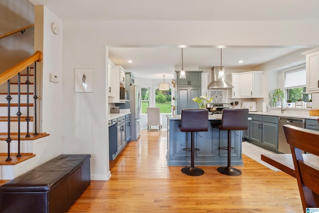 2616 Chimney Hills Cir, Vestavia Hills, AL 35226 - kitchen with wall chimney range hood, light wood-style floors, light countertops, a breakfast bar area, and stainless steel appliances