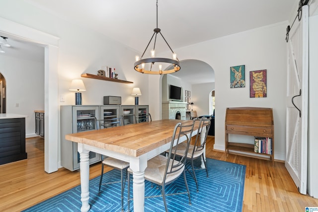 dining space with arched walkways, light wood-type flooring, a chandelier, crown molding, and a barn door