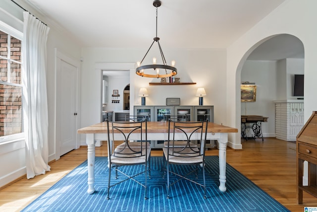 dining area featuring wood finished floors, arched walkways, a chandelier, and baseboards