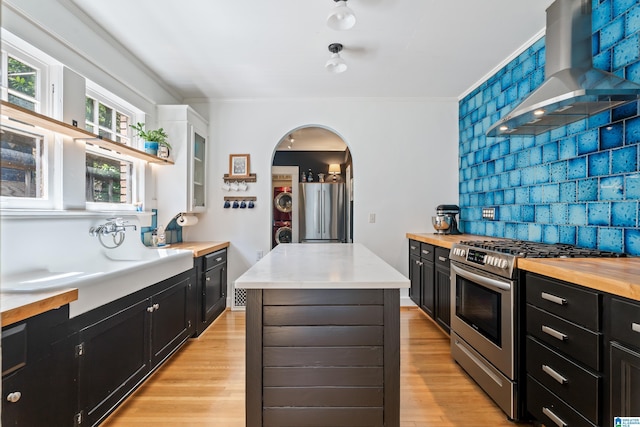 kitchen featuring appliances with stainless steel finishes, wall chimney range hood, dark cabinets, and ornamental molding
