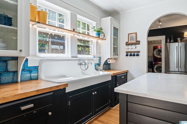 kitchen with high quality fridge, stacked washer / drying machine, wood counters, dark cabinets, and ornamental molding