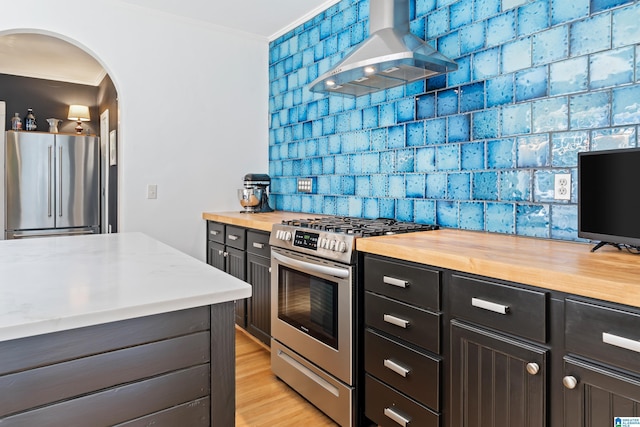 kitchen with appliances with stainless steel finishes, ventilation hood, arched walkways, wooden counters, and crown molding