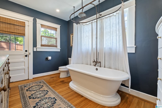 bathroom featuring baseboards, a freestanding tub, wood finished floors, toilet, and a shower with shower curtain