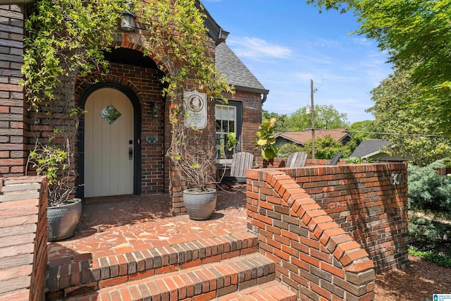 entrance to property with brick siding and a shingled roof