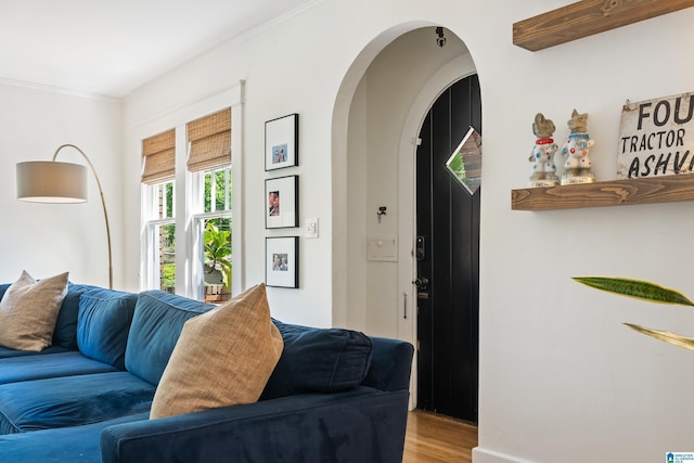 living area with arched walkways, wood finished floors, and ornamental molding