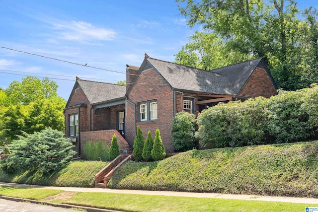 view of front of property featuring brick siding, a shingled roof, a chimney, and stairway
