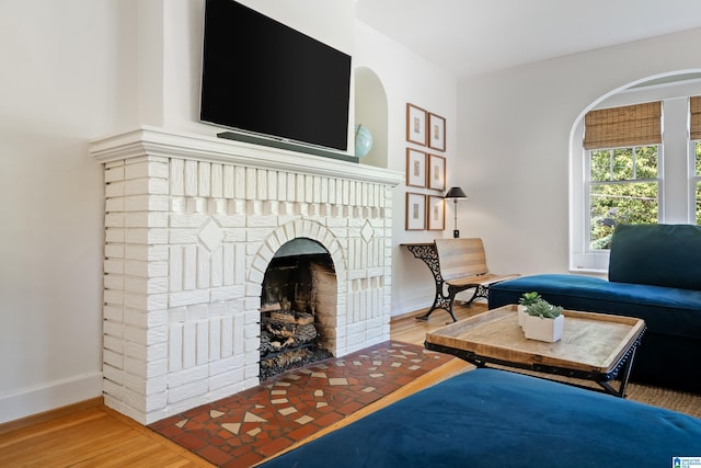 living area with wood finished floors, a brick fireplace, and baseboards